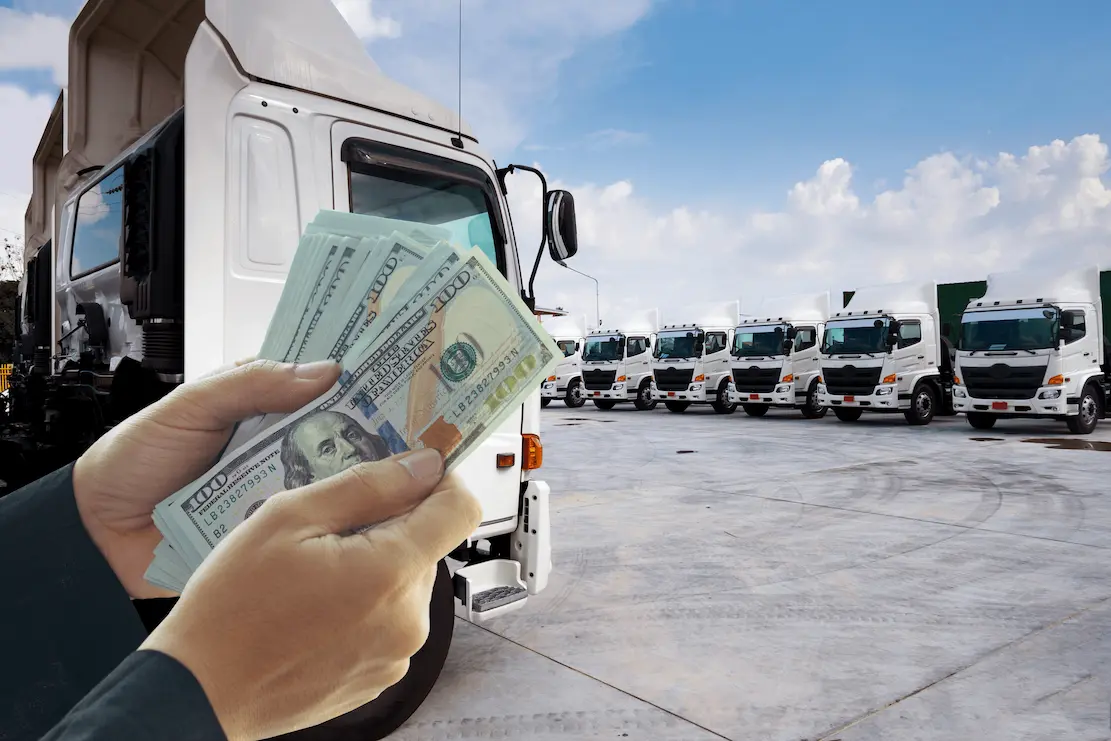 Person holding money with trucks in the background
